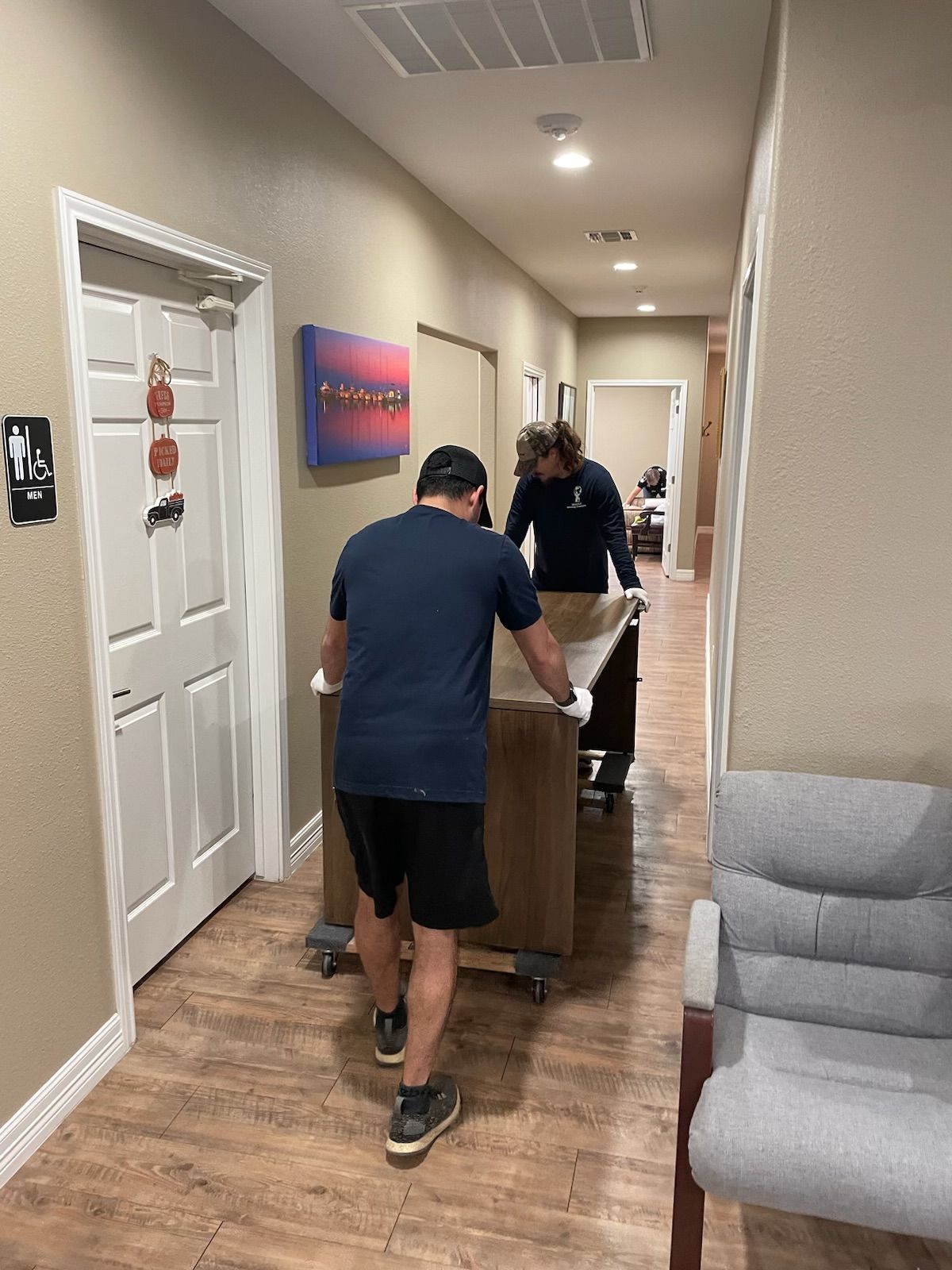 Two people moving a large box on a dolly down a hallway.