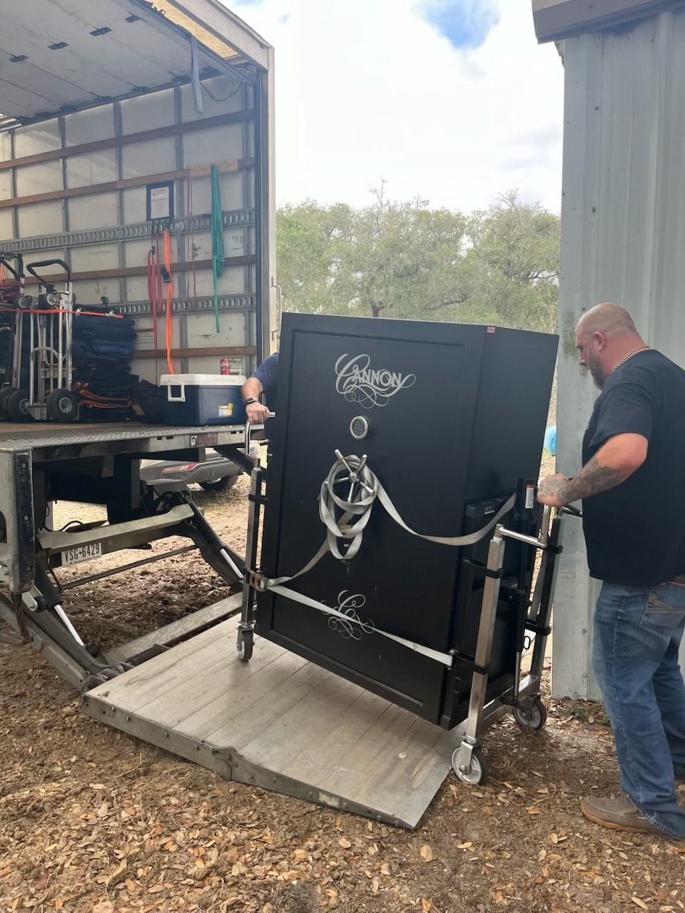 A person rolling a large black safe on wheels out of a moving truck onto a ramp.