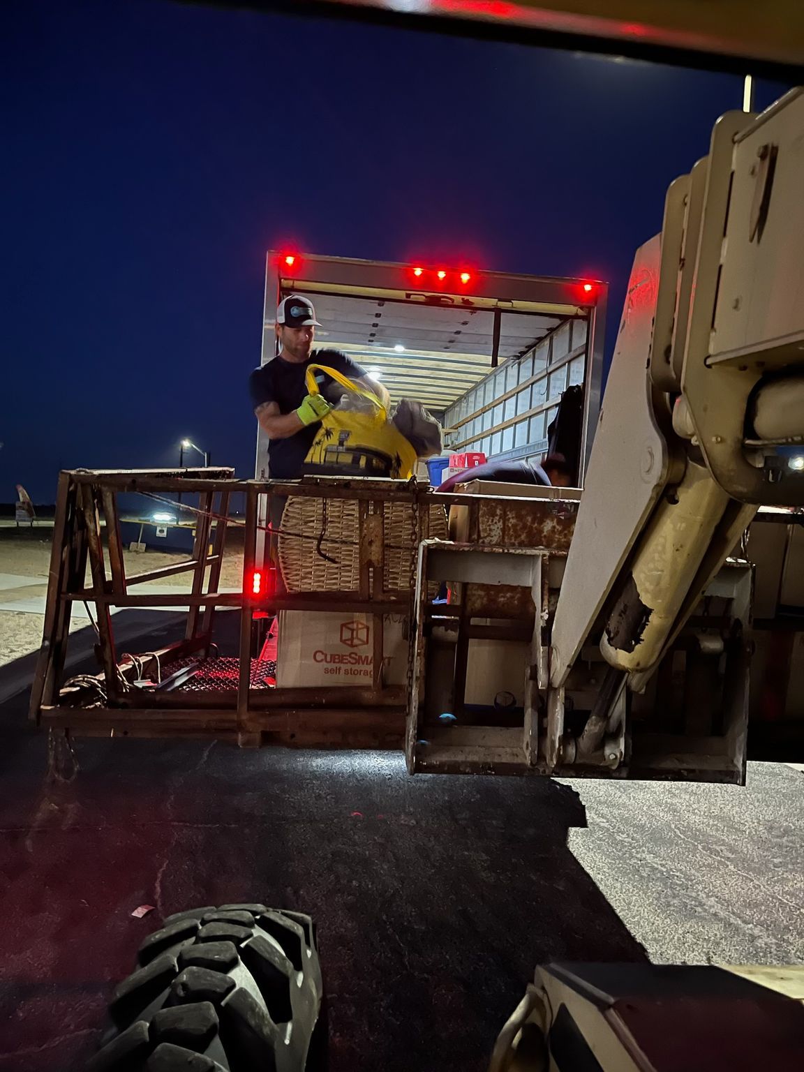 Man loading a yellow machine into a truck at dusk.