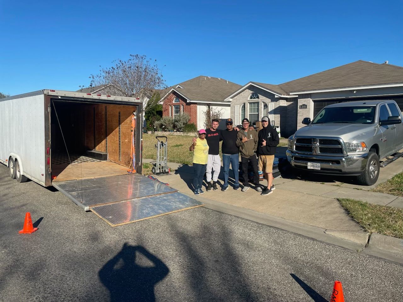 Five people stand near a trailer and truck in a driveway on a sunny day.
