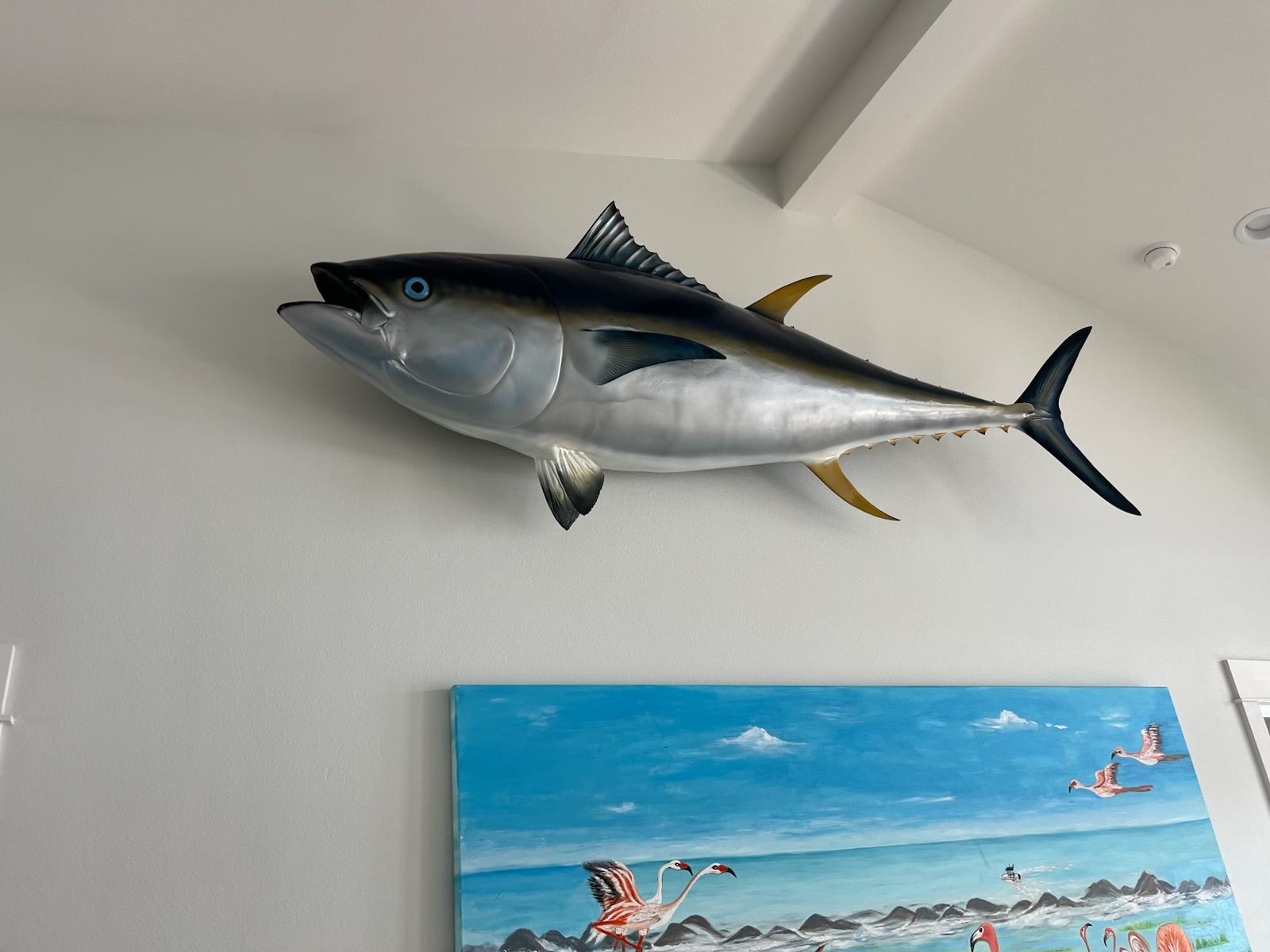 Large tuna fish mount on a white wall above a colorful seascape painting.