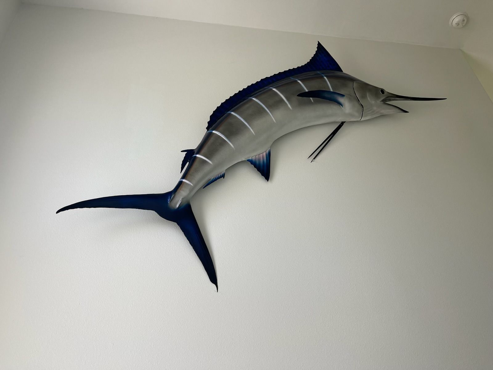 Metal blue marlin sculpture mounted on a white wall.