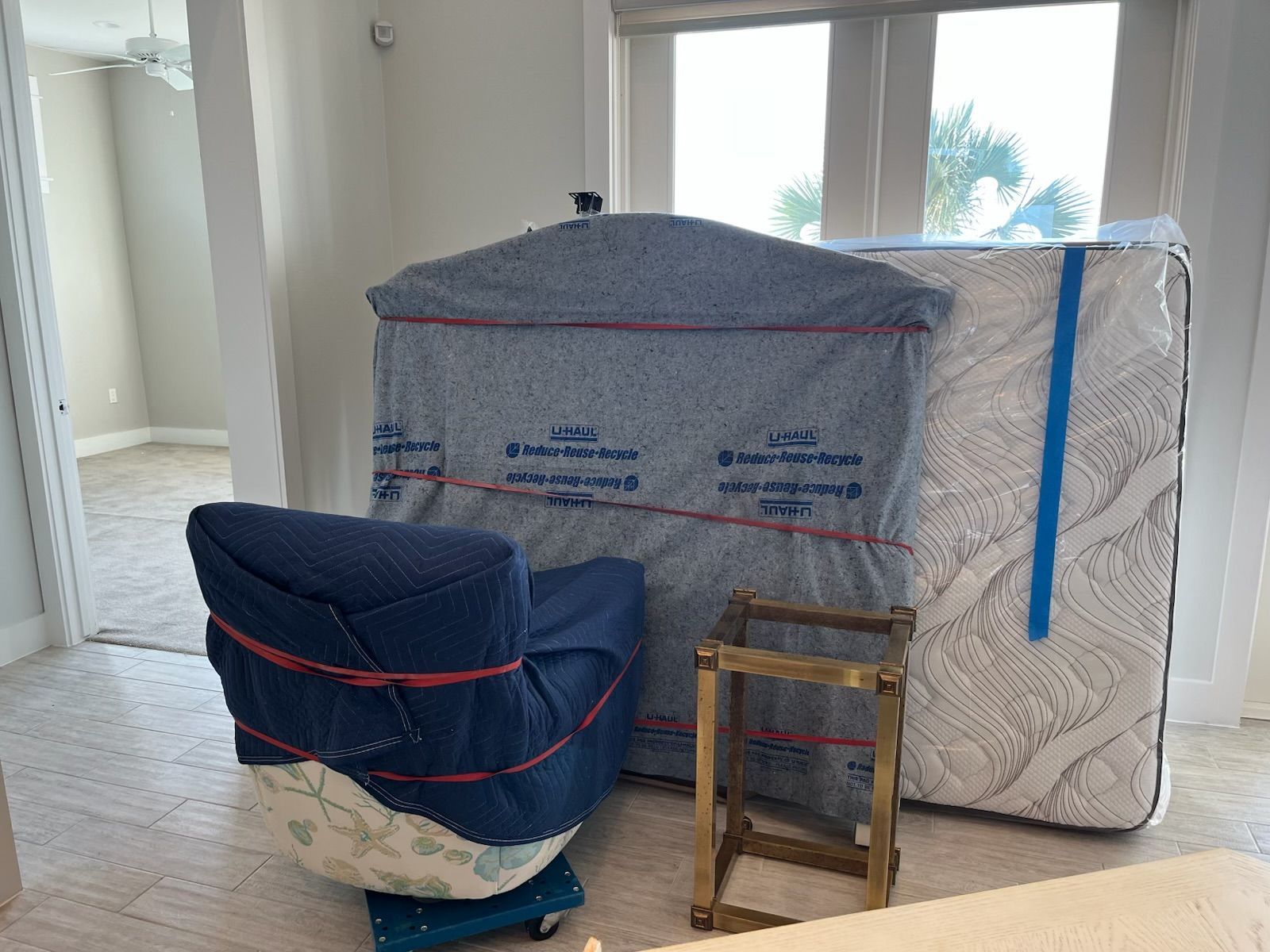 Moving supplies: wrapped chair, headboard, mattress, small frame, in a room.