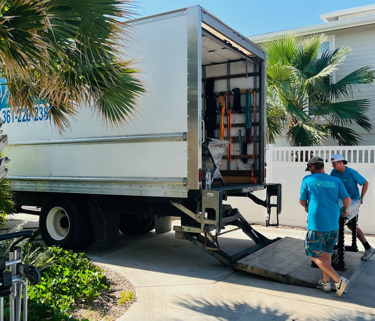 Moving truck with ramp down; two men loading boxes, sunny residential setting.