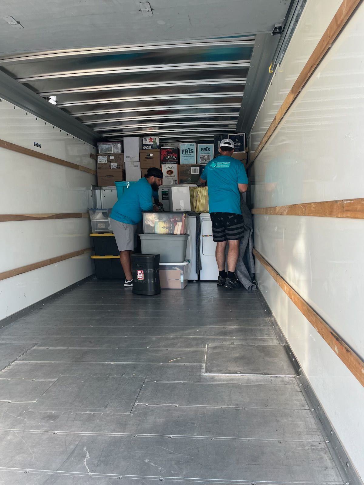 Two movers loading boxes into a truck, inside view.