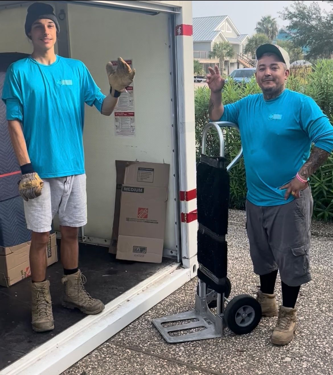 Two men in turquoise shirts near a truck, one holds a glove. They are smiling.