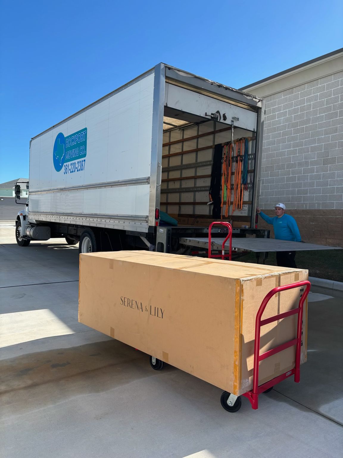 Moving truck with open door; large cardboard box on a dolly. Person loading items.