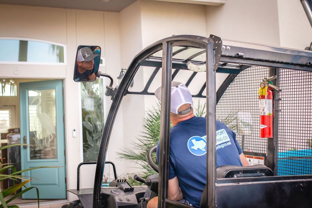 Man driving a forklift near a house; blue door visible.