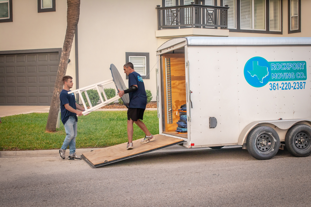 Two men loading items into a moving trailer on a residential street.