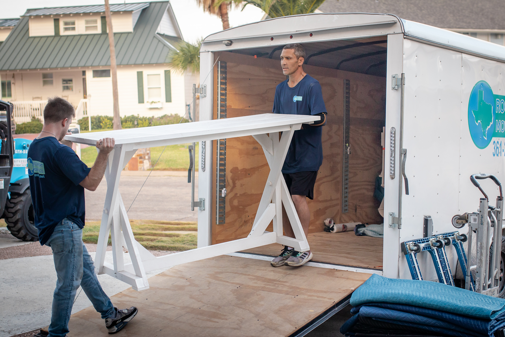 Two movers load a white table into a white moving trailer.