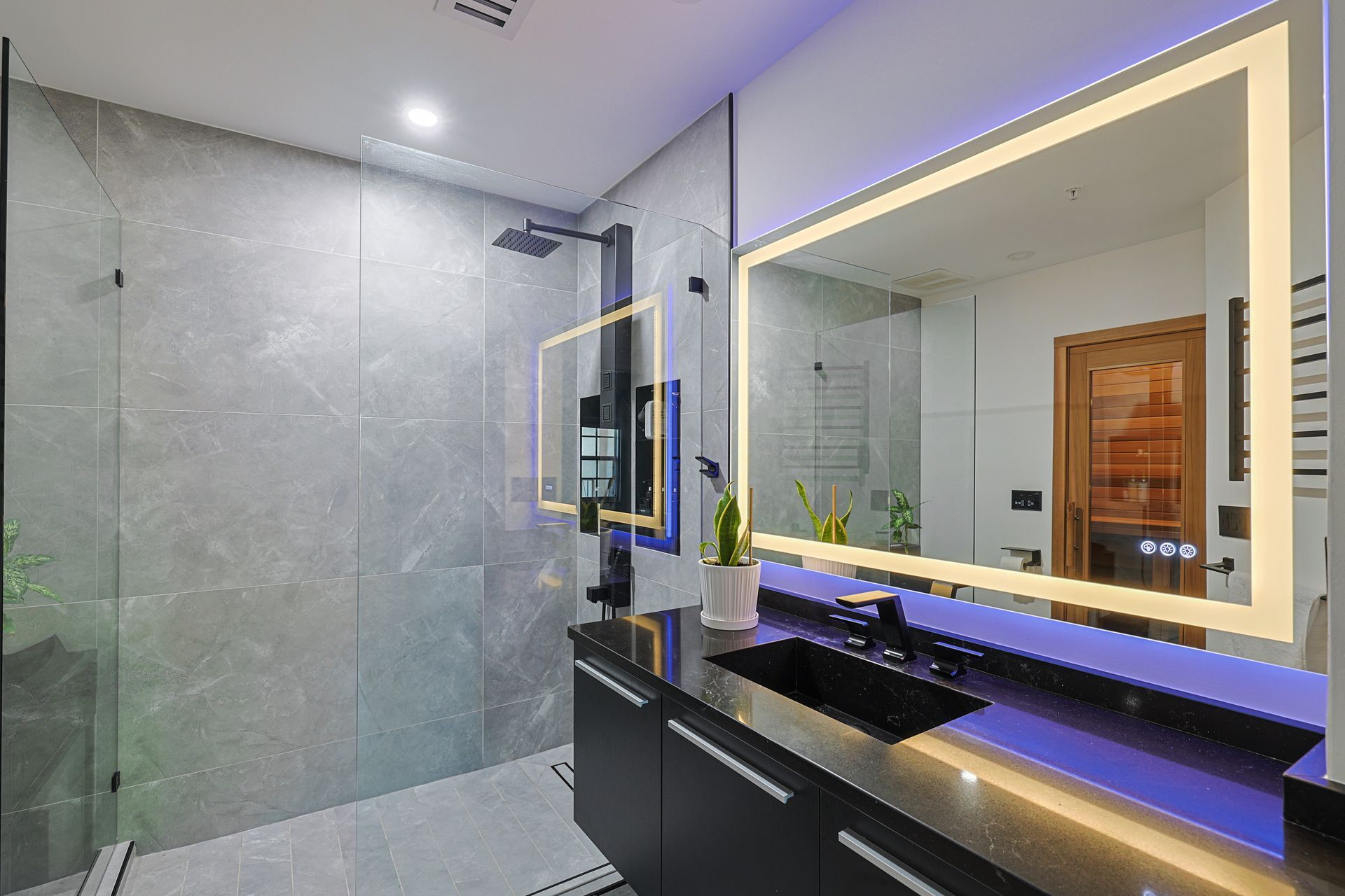 Modern bathroom with black vanity, large mirrors with LED lighting, and a gray tiled shower.