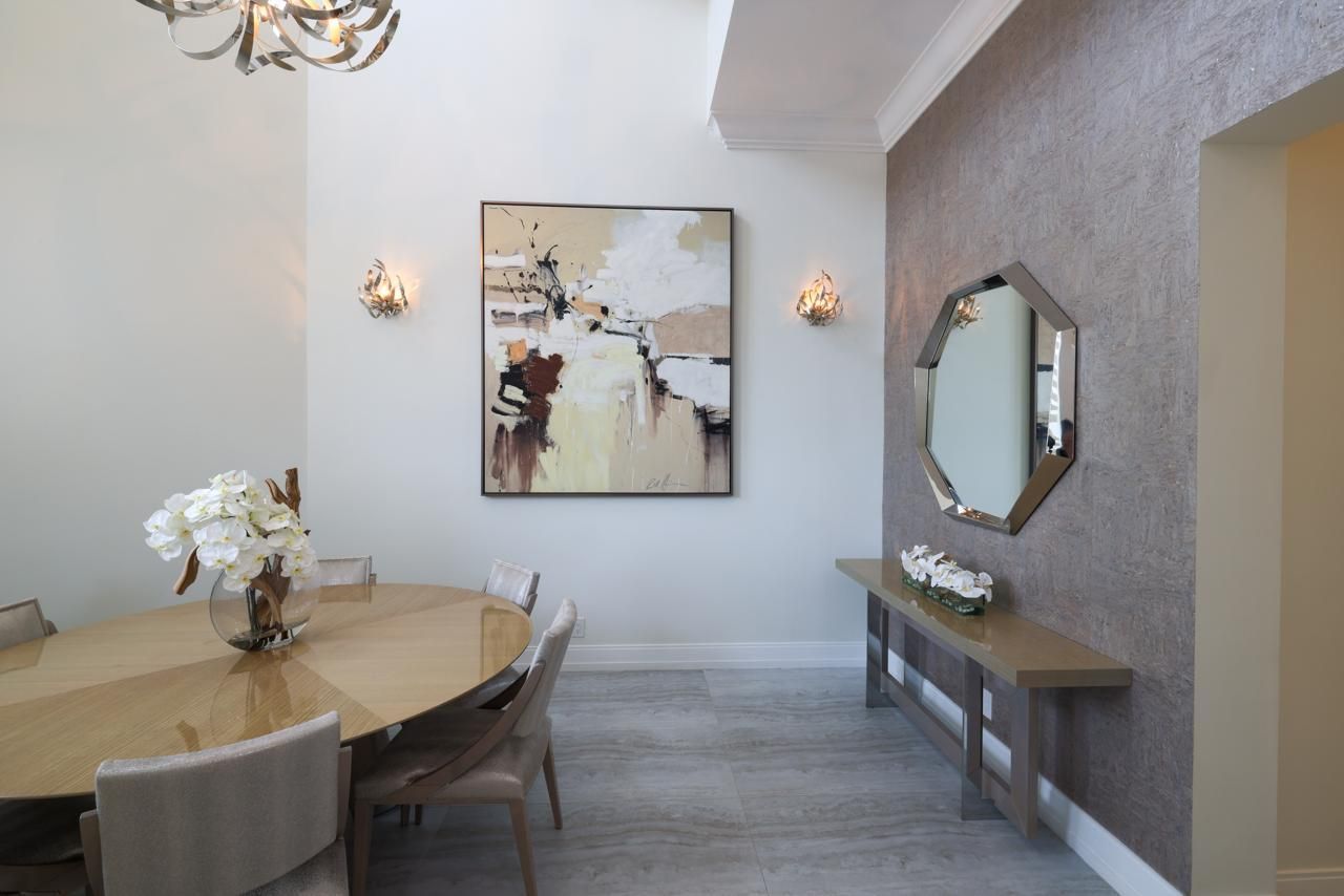 Elegant dining room with a round wooden table, art, and an octagonal mirror on a textured wall.