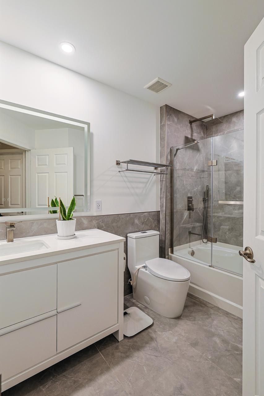 Modern bathroom with white vanity, toilet, and shower with gray walls and floor.