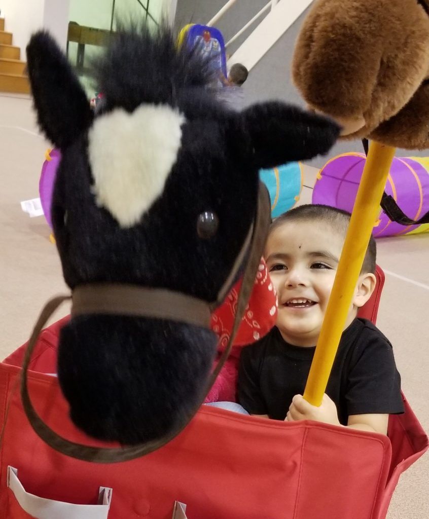 A little boy is holding a stick in front of a stuffed horse