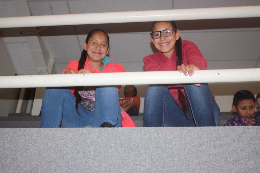 Two girls are sitting on a balcony looking over a railing.