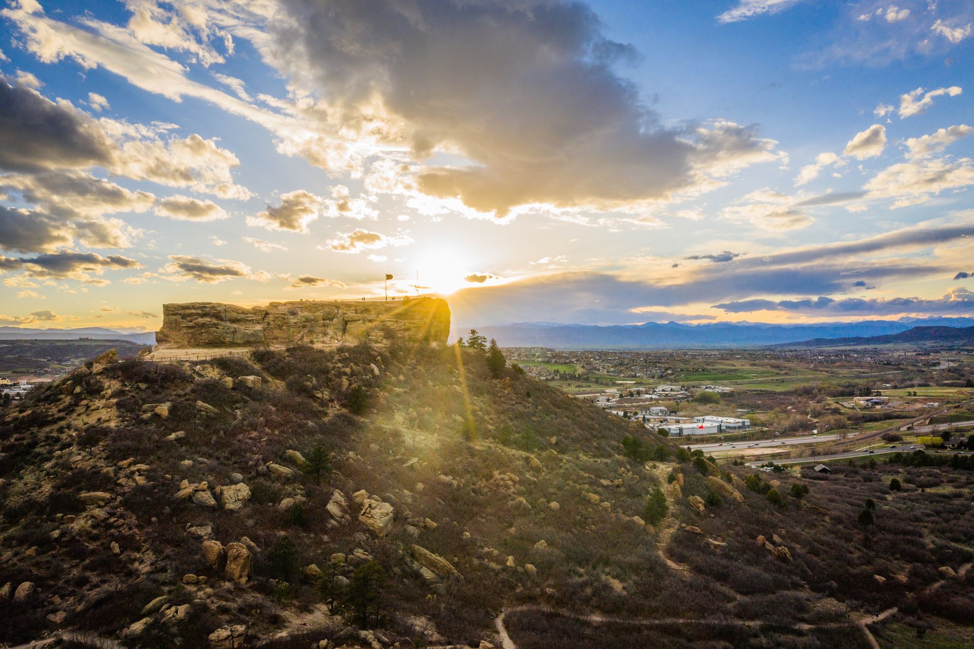 Sunset over a rocky hilltop overlooking a valley, with golden clouds and distant mountains