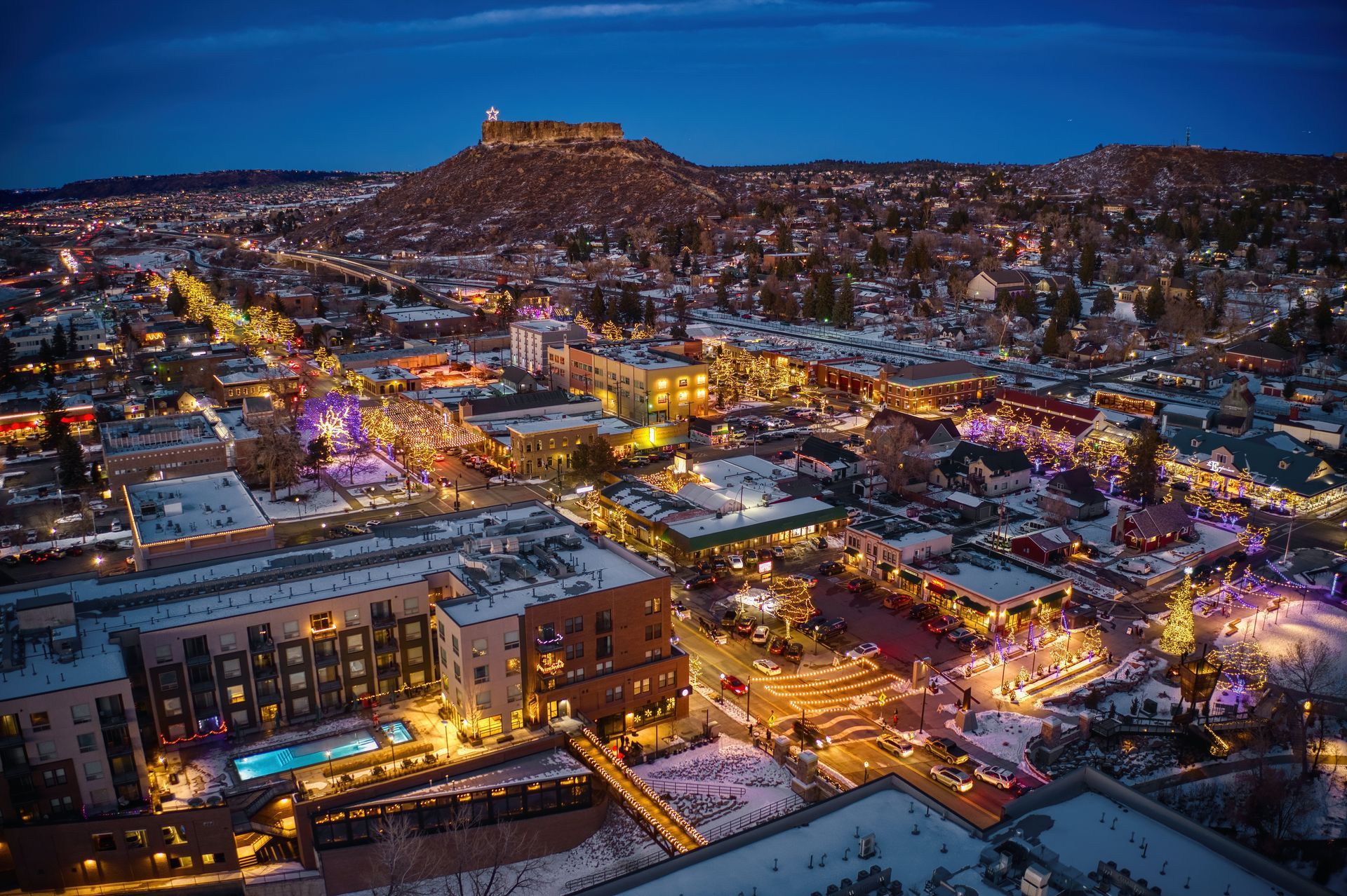 Nighttime cityscape with glowing streets and buildings beneath a hilltop fortress.