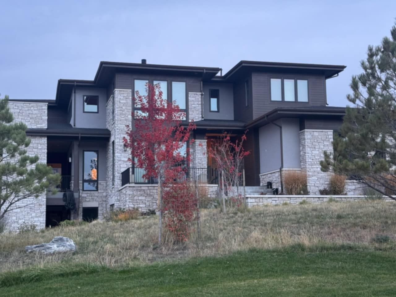 Modern house with stone and dark wood exterior on a grassy hill.