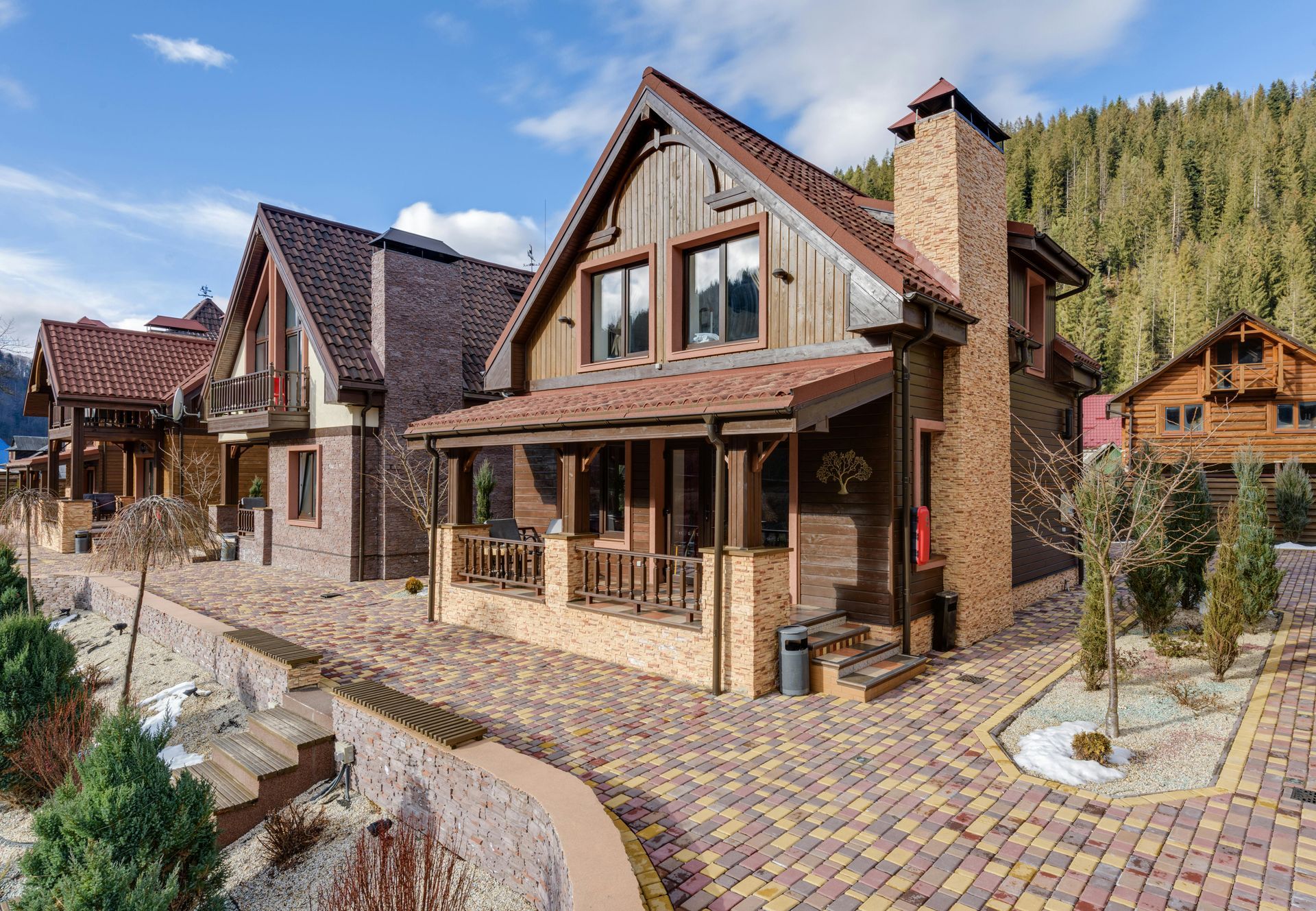 Row of brown and brick houses with gabled roofs, a cobblestone walkway, and a forested hillside.