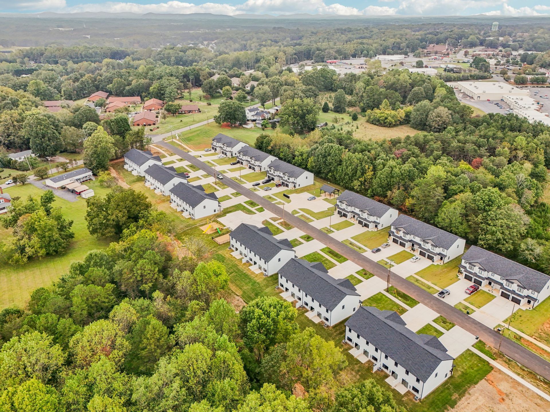 Aerial view of a row of modern townhomes with black roofs and white exteriors in a green, wooded area.