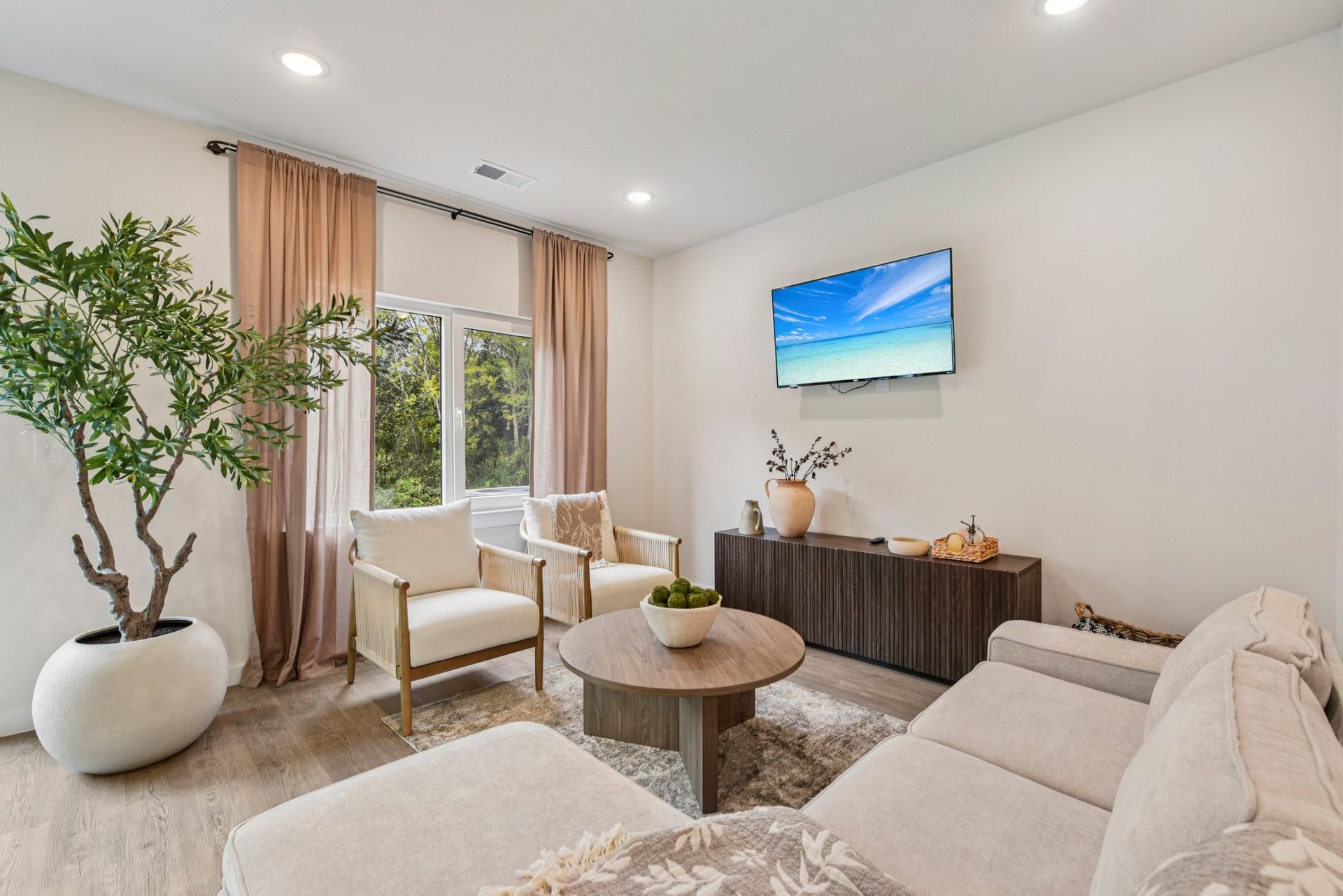 Living room with beige sofa, chairs, and tree. TV mounted on wall.