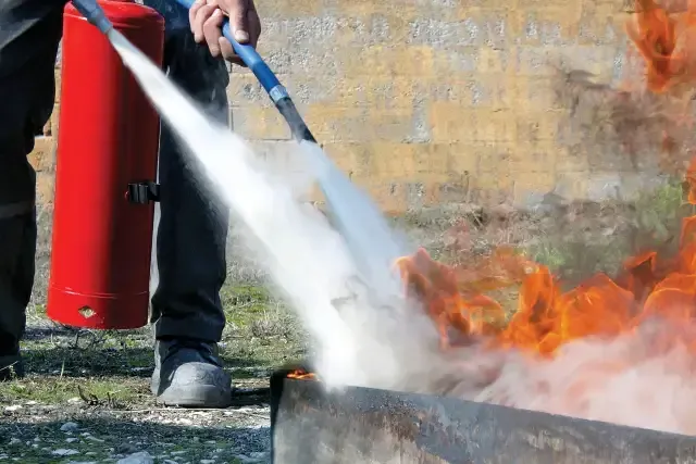 Person using a fire extinguisher to put out flames in a burning container outdoors