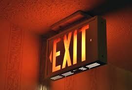 Illuminated EXIT sign glowing orange on a wall in a dim hallway