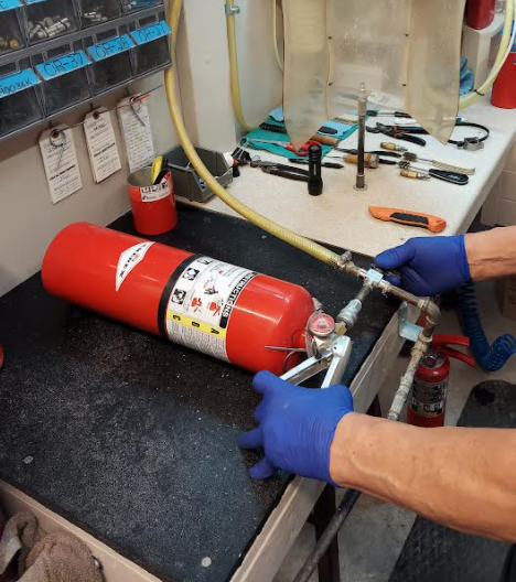 Technician in blue gloves handling a red fire extinguisher on a workbench in a workshop