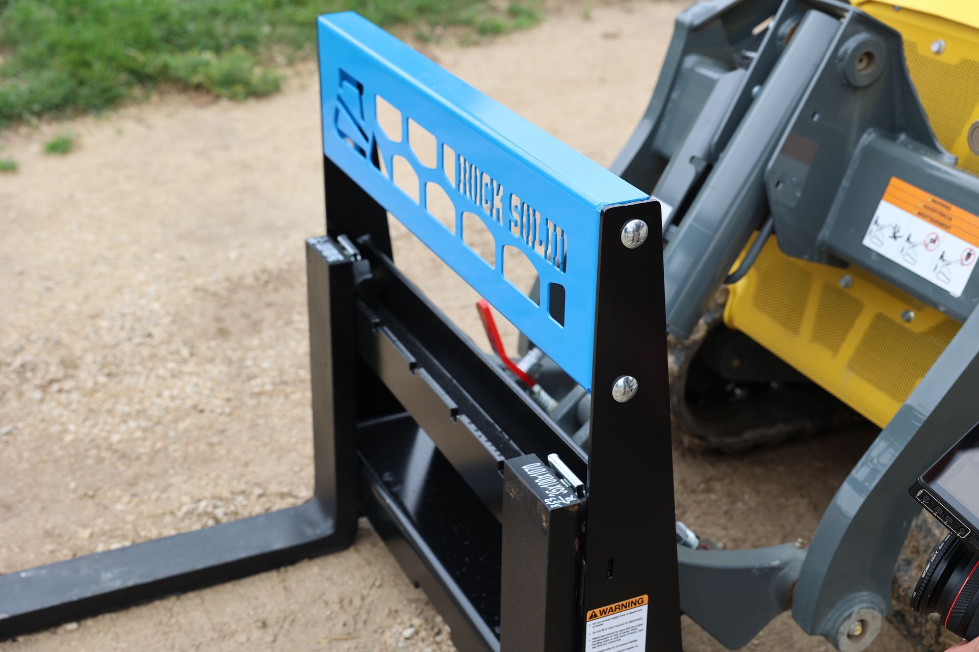 A blue and black forklift is sitting next to a yellow tractor.