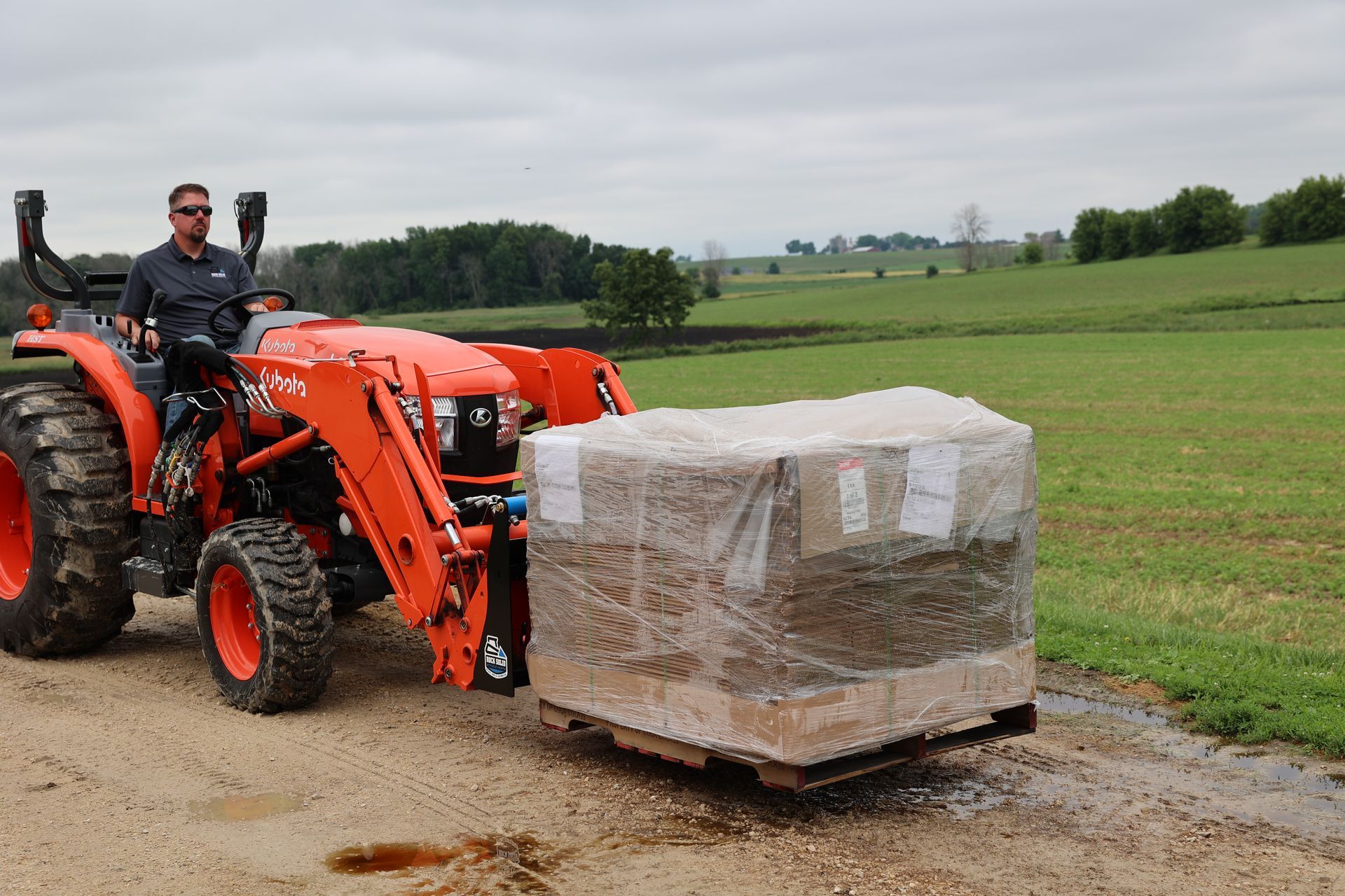 A man is driving a tractor with a pallet of boxes on it.