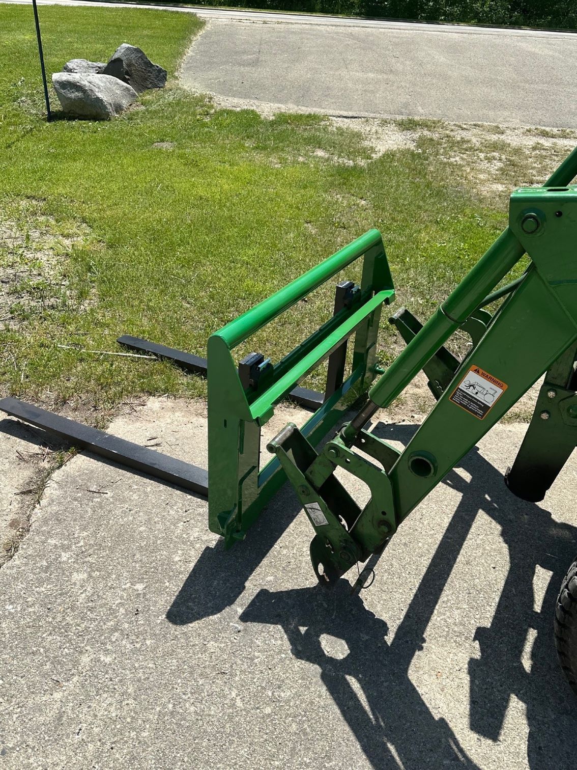 A green tractor with forks attached to it is parked on the side of the road.