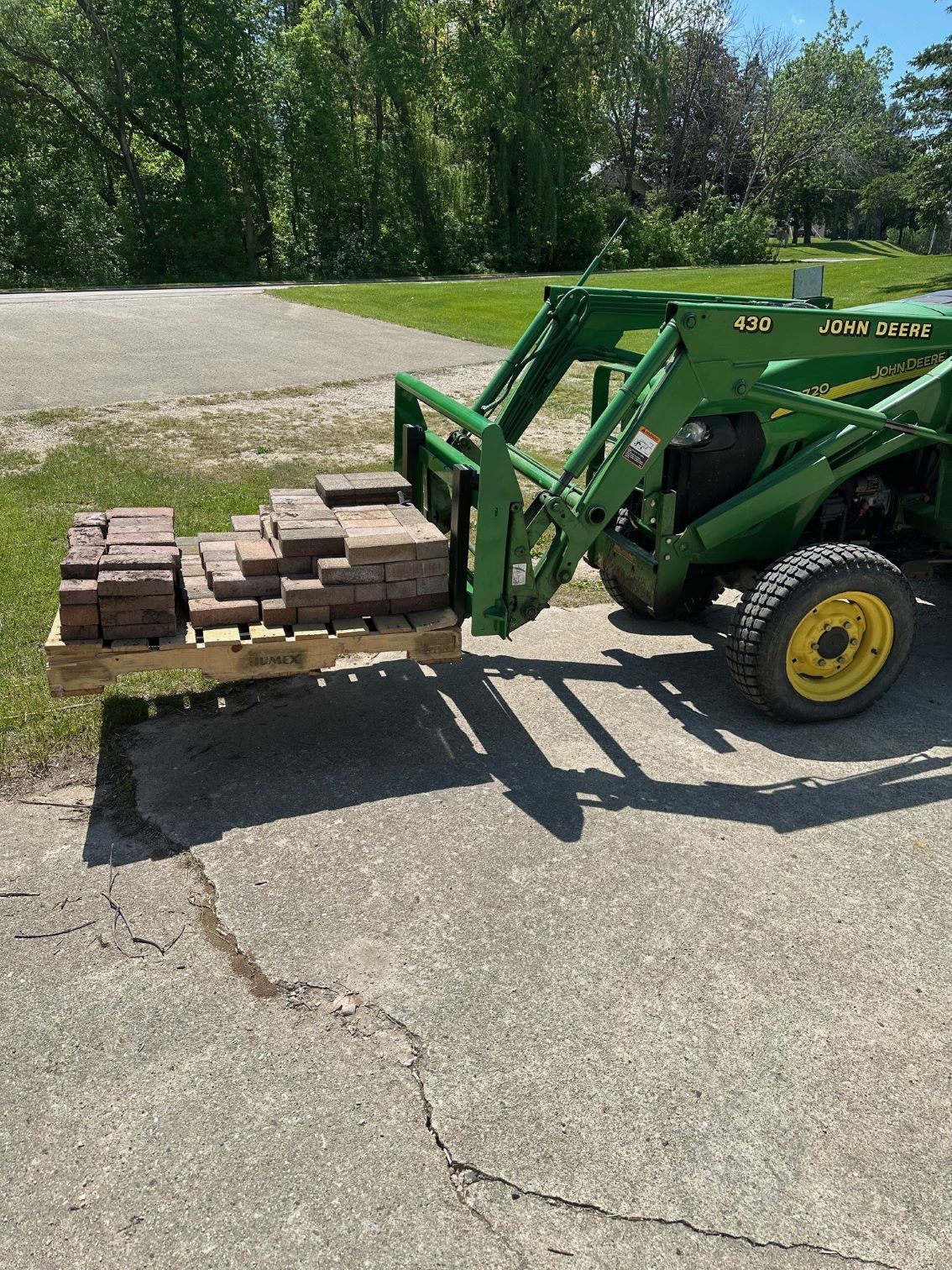 A green tractor is pulling a pallet of bricks.