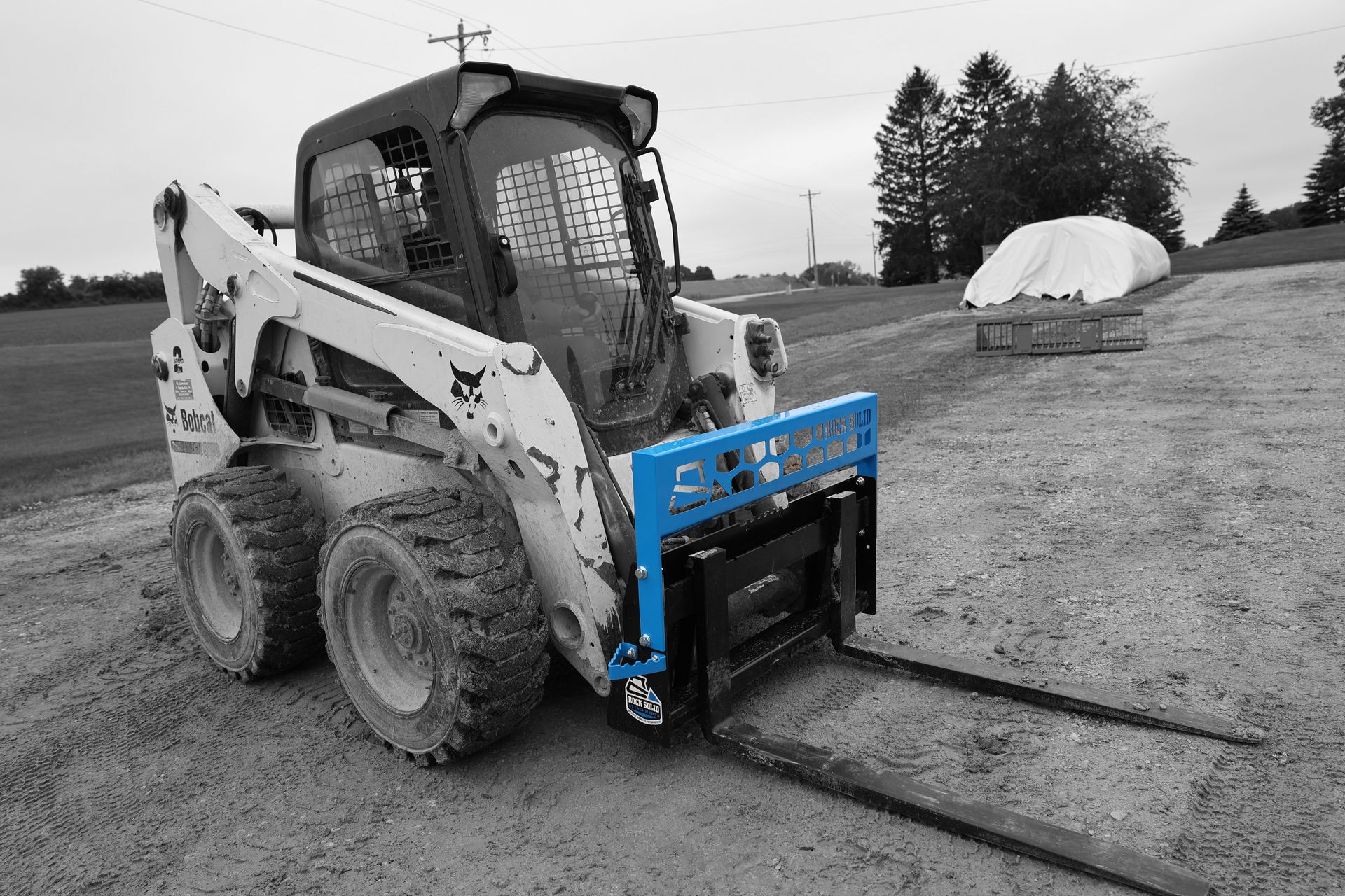 A black and white photo of a bobcat with a blue forklift attached to it.