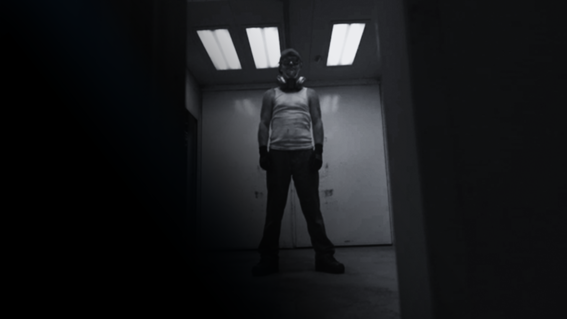 A man wearing a gas mask is standing in a dark room.