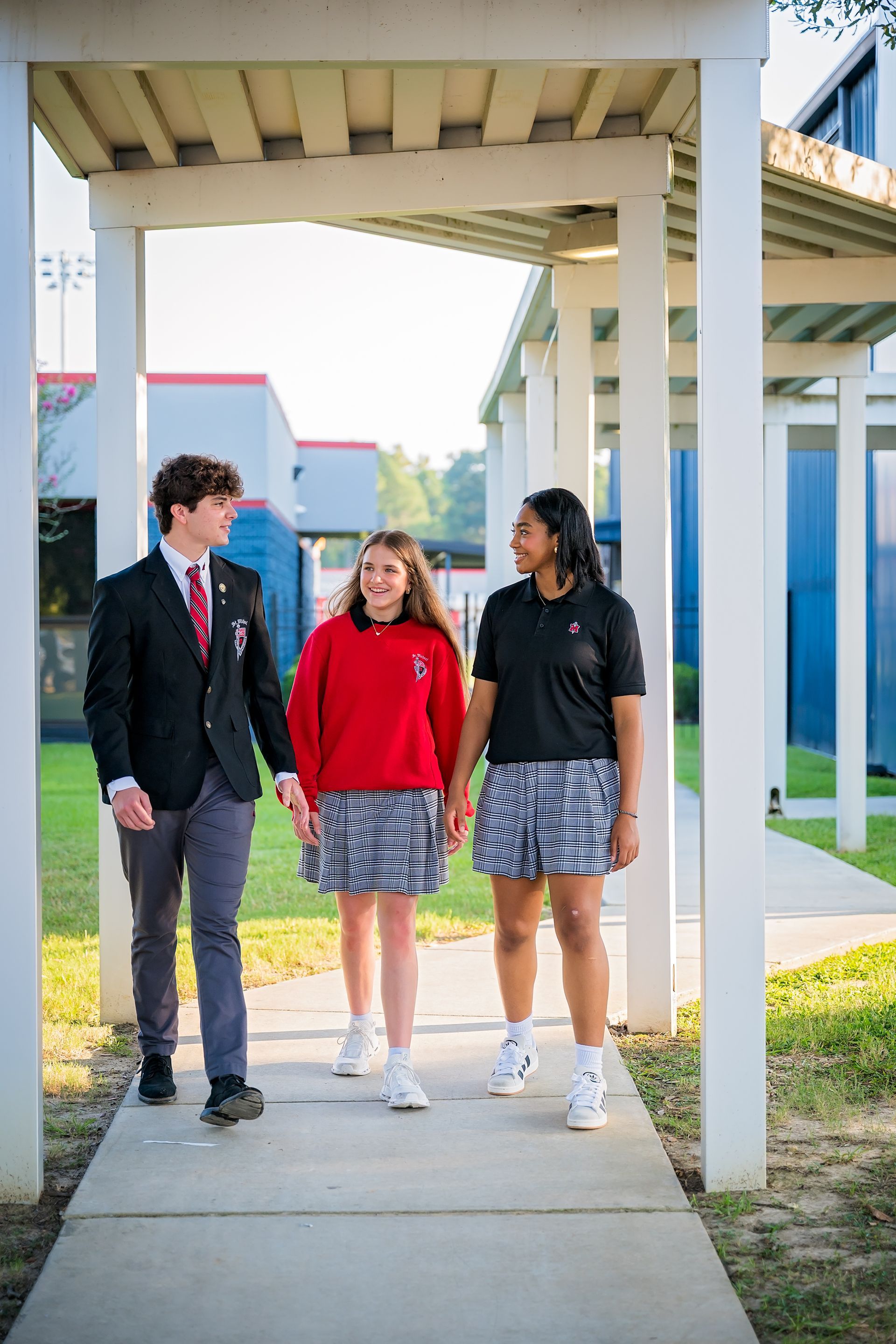 Three students walking under a covered outdoor walkway at a school campus.