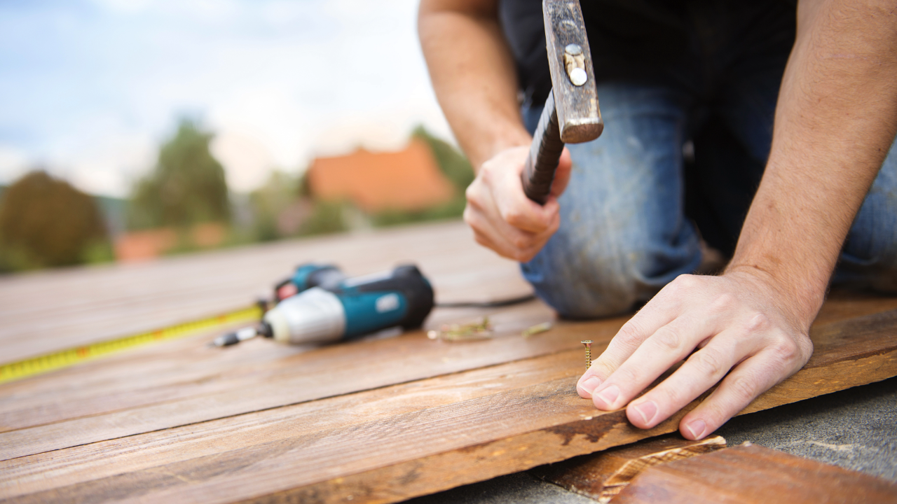 A plumber is standing in a kitchen holding a drill and pliers.
