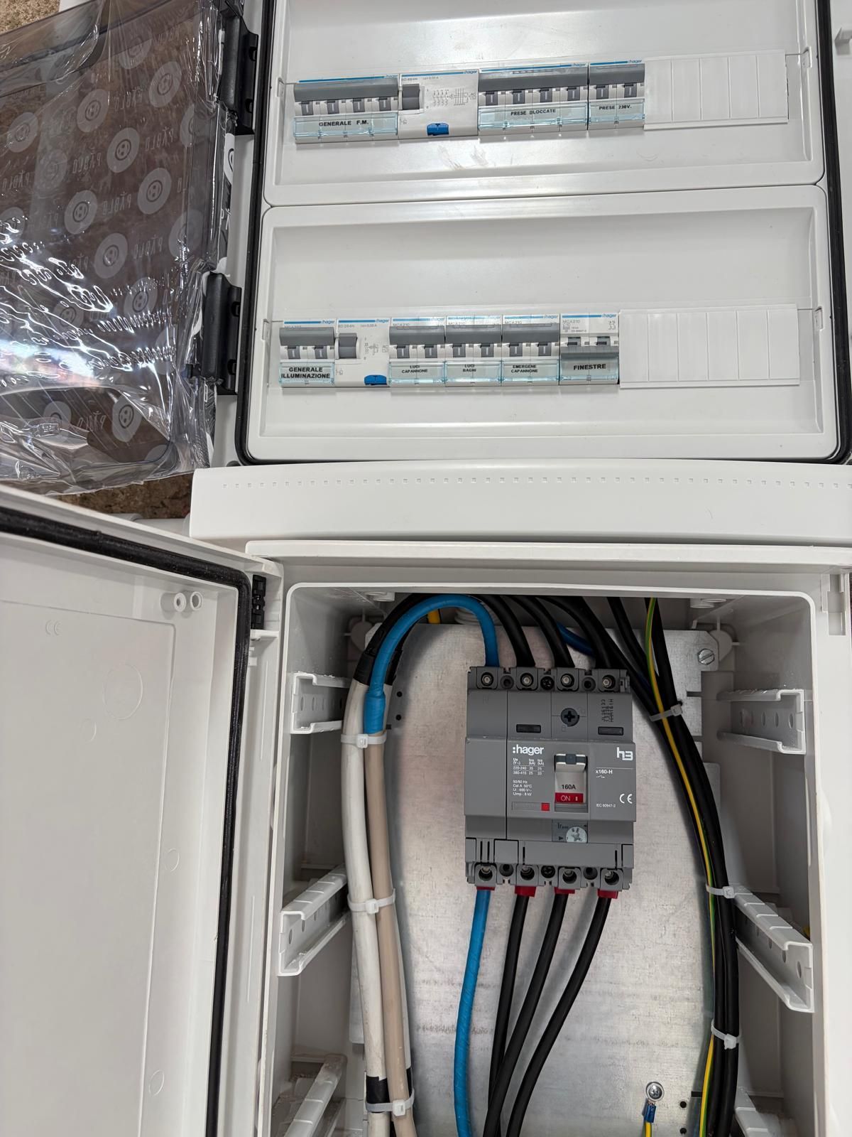 Quadro elettrico aperto con interruttori e cablaggio, inclusi cavi blu e neri all'interno di un armadio bianco.