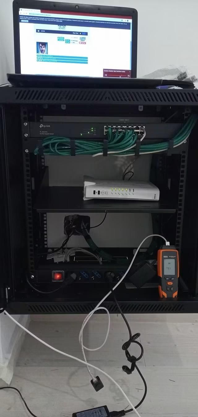 Rack per server aperto con un laptop sopra e apparecchiature di rete all'interno, con cavi pendenti.