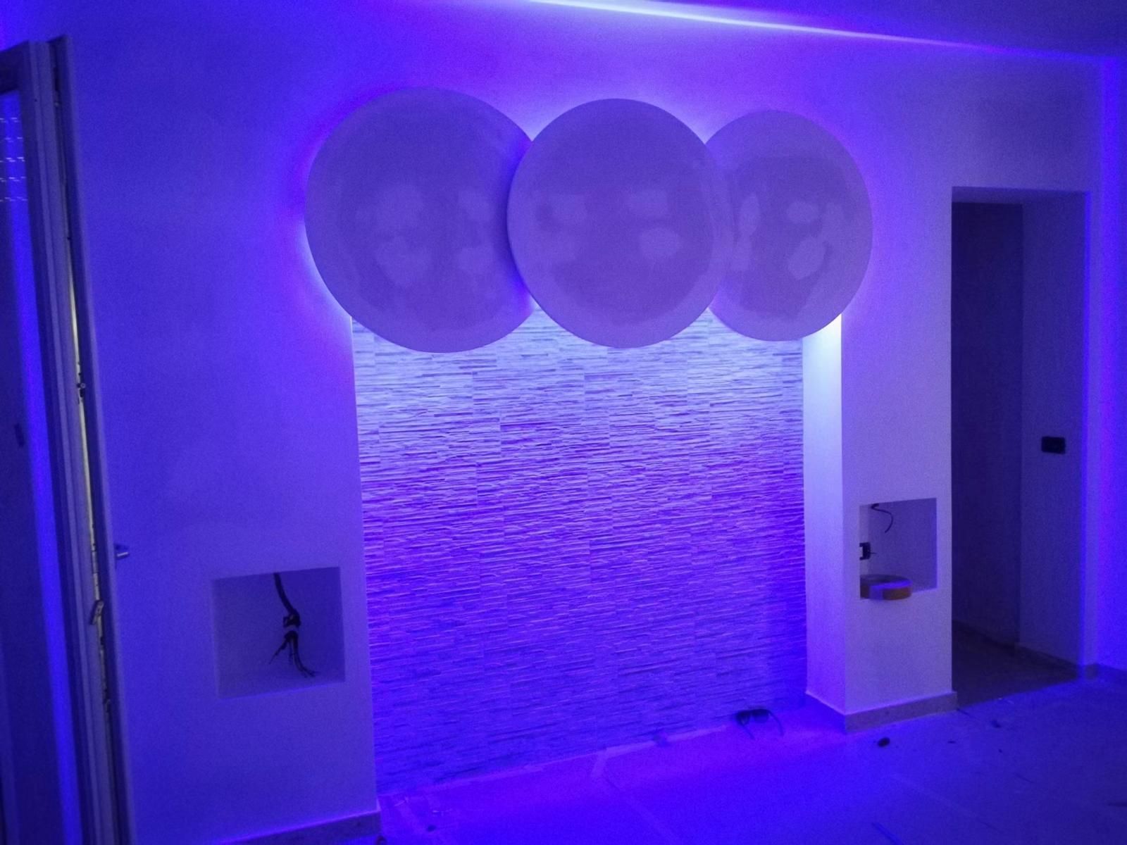 Fontana a muro illuminata di viola con tre pannelli decorativi rotondi sopra di essa