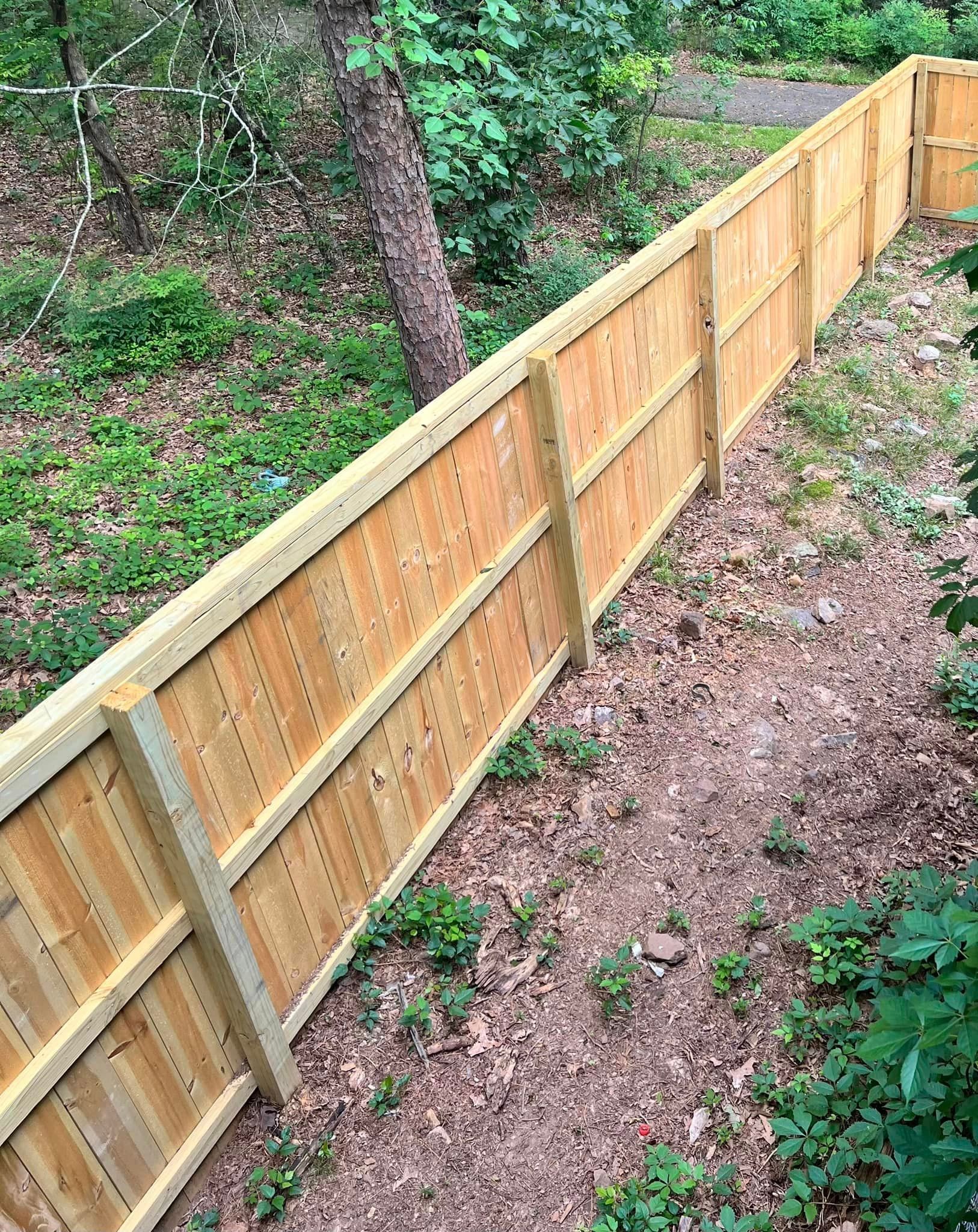 A wooden fence is surrounded by trees and grass in a yard.