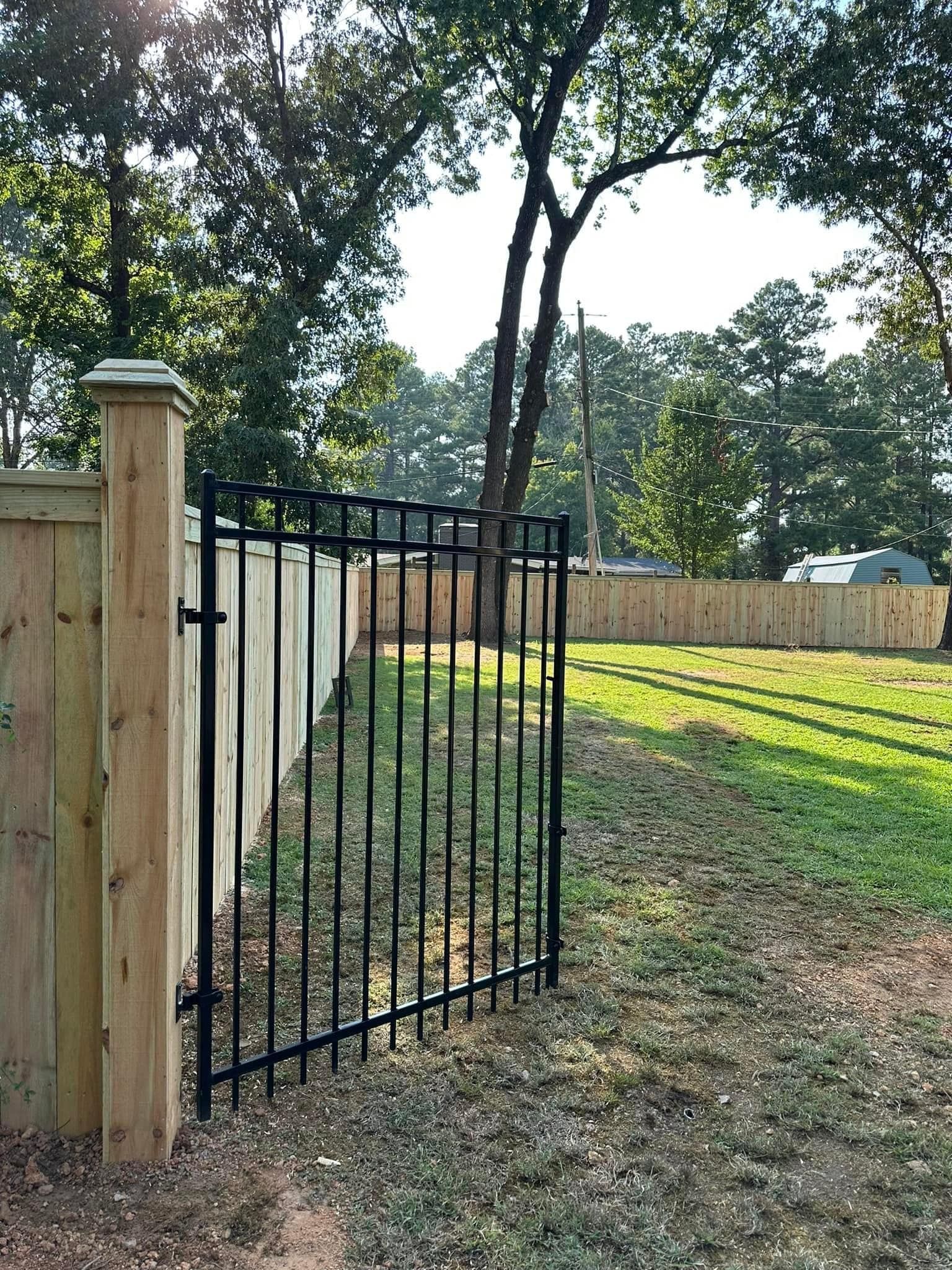 A wooden fence with a metal gate and a tree in the background.