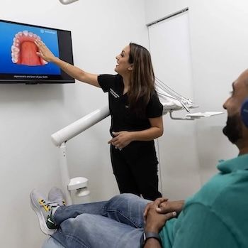 Dentist showing a patient a 3D model of teeth on a screen in a dental office.