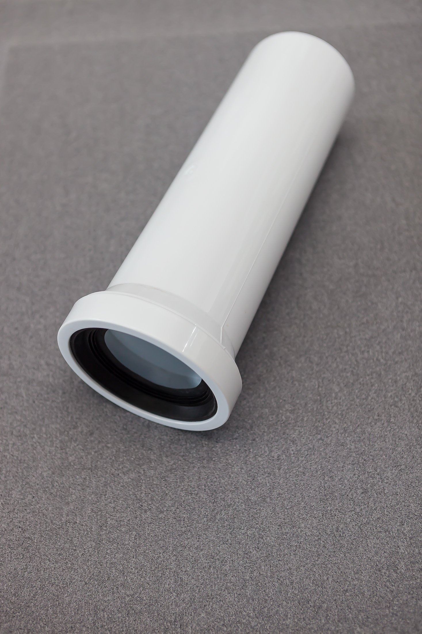 Tubo cilindrico di plastica bianca con bordo svasato, appoggiato su una superficie grigia ruvida.