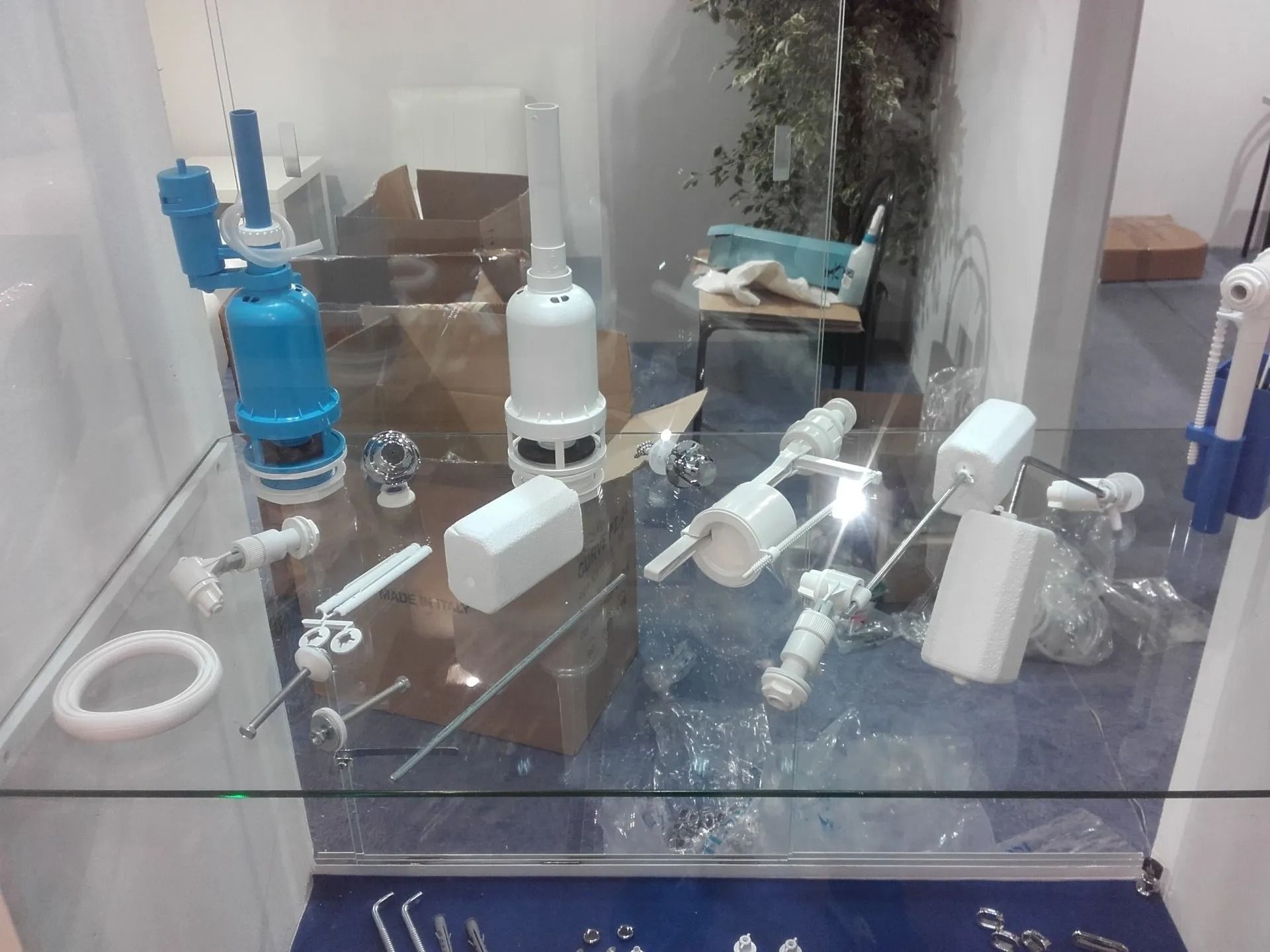 Lavabo del bagno ingombrato da spazzolini da denti, flaconi e articoli da toeletta dietro un pannello di vetro a specchio.