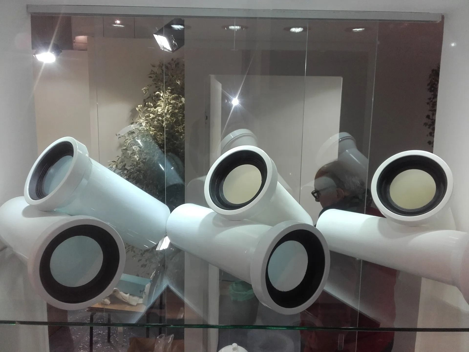 Grandi tubi scultorei bianchi con aperture circolari nere esposti in una vetrina.