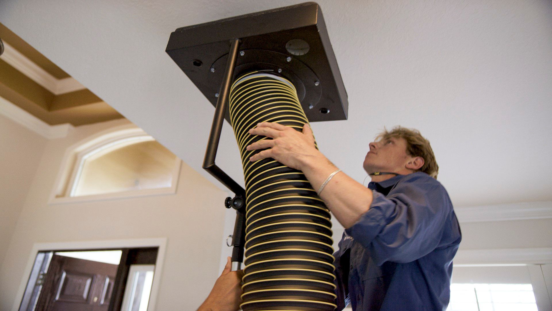 Person installing a large black spiral duct into the ceiling in a home interior