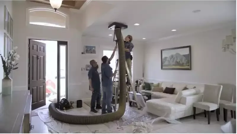 Workers installing a large coiled duct in a bright living room with white furniture