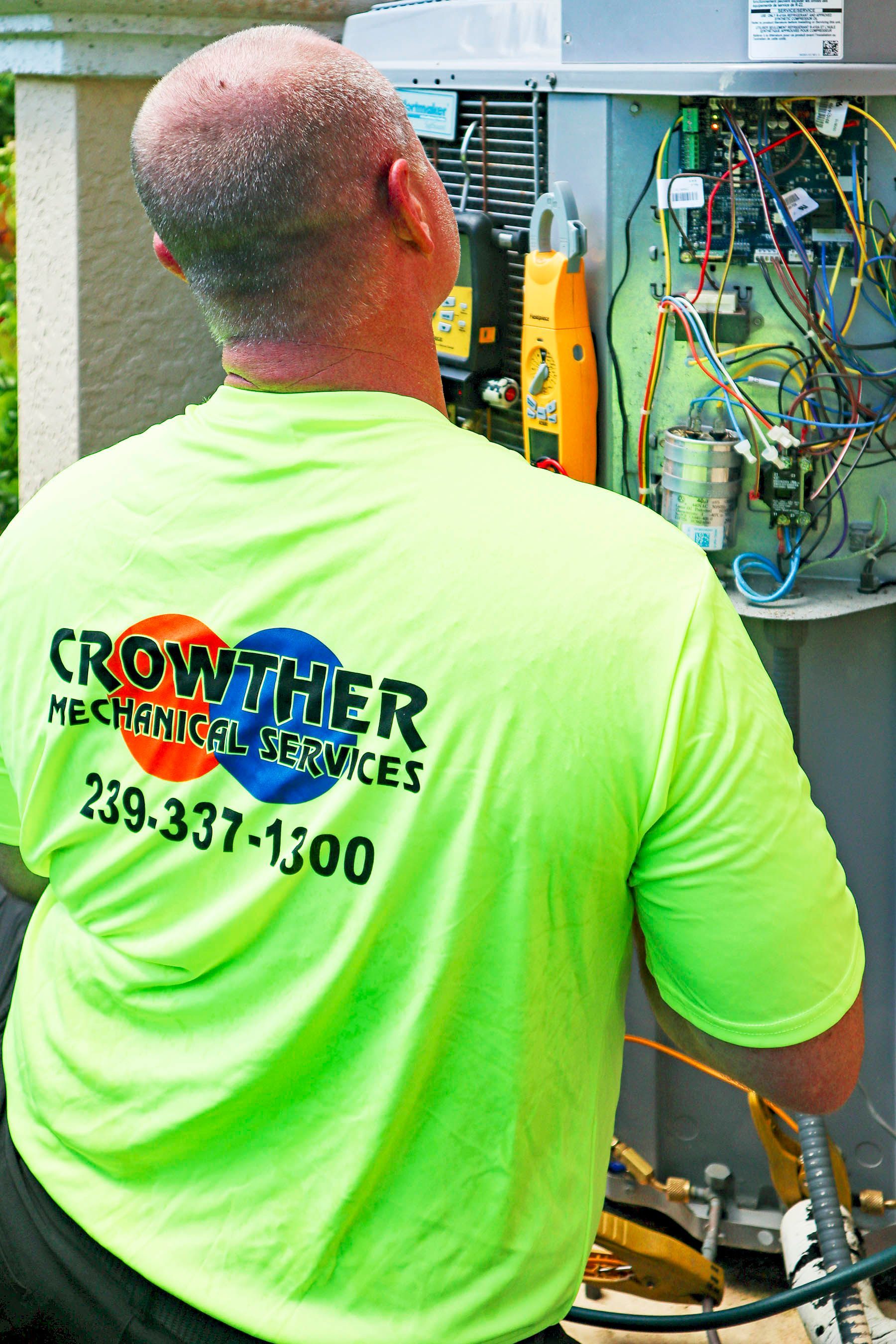 Technician in neon green shirt working inside an open electrical panel outdoors