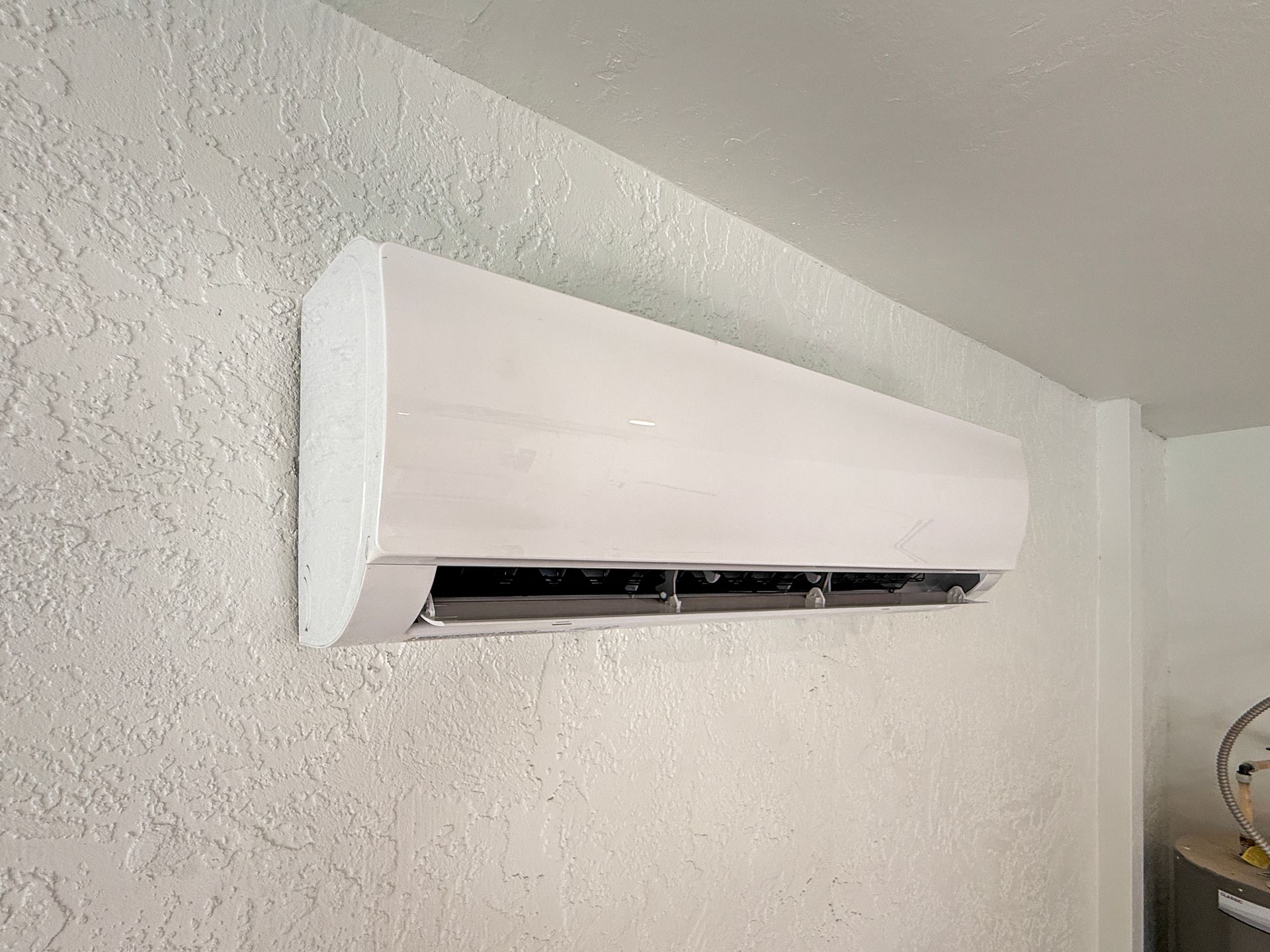 White wall-mounted air conditioner on an indoor wall with open lower vent slats