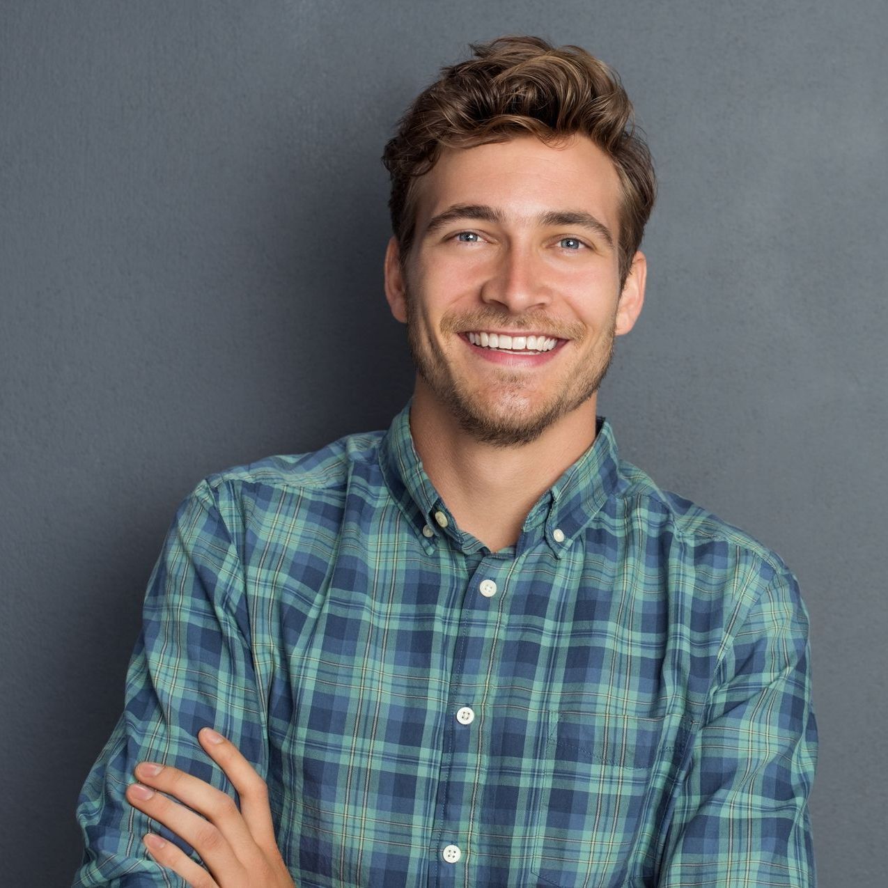 A man in a plaid shirt is smiling with his arms crossed.